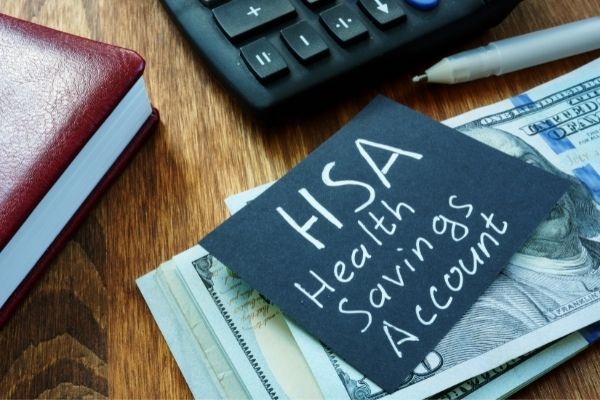 Black paper with white written text "HSA Health Savings Account" on top of money.